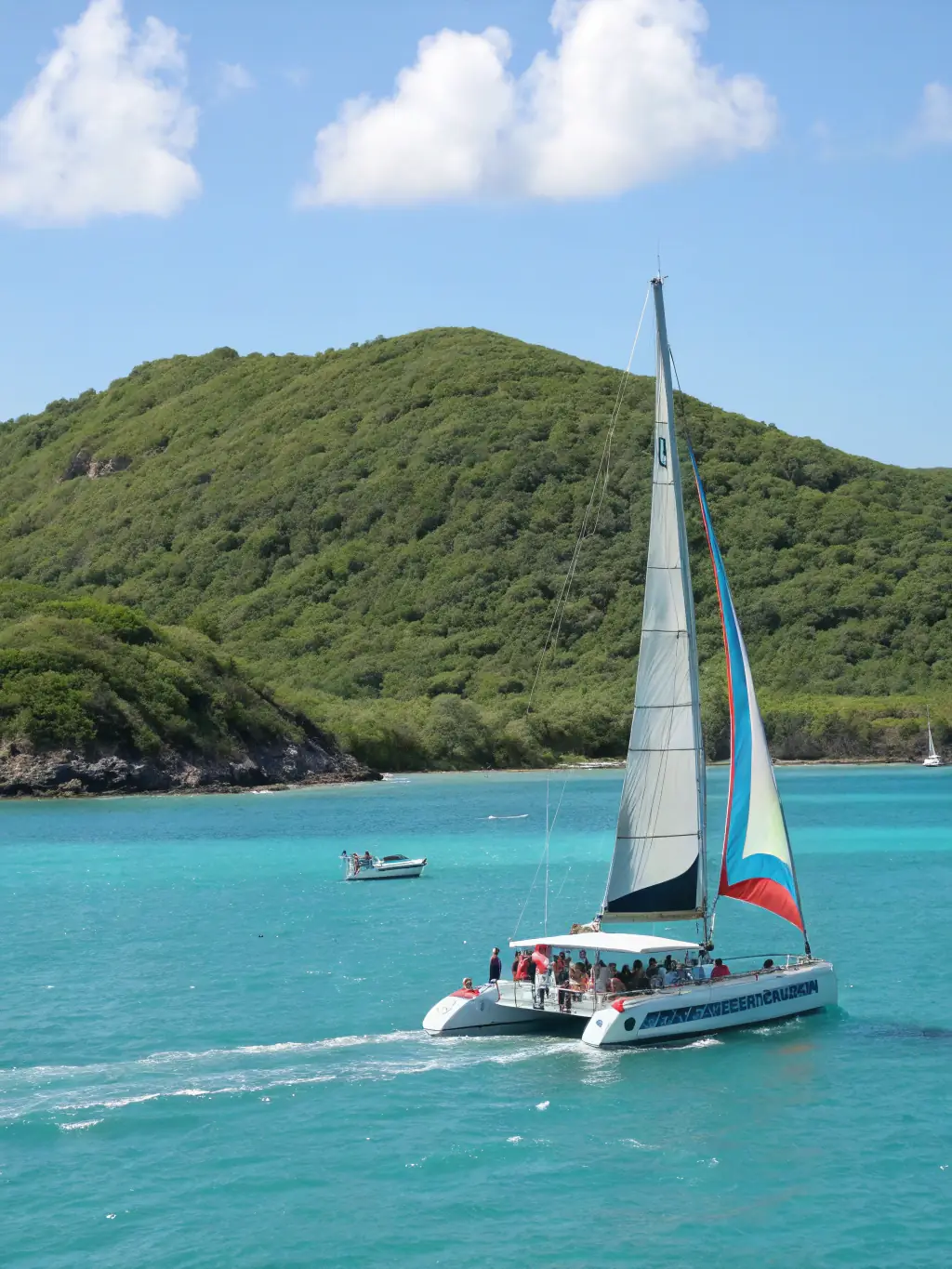 A vibrant image of a catamaran sailing on the turquoise waters around Nosy Sakatia, with tourists enjoying the sun and scenery during a day trip.